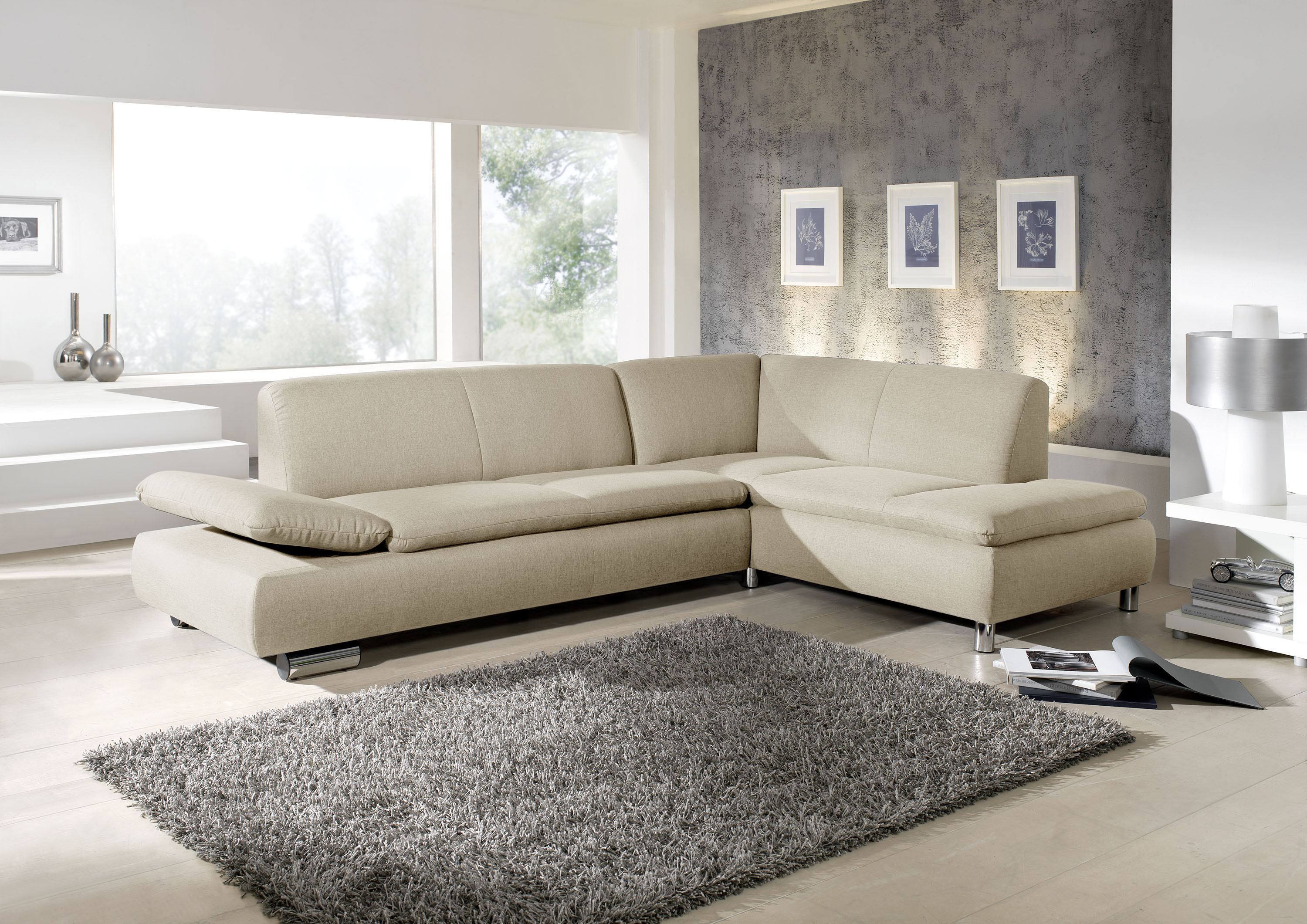 modernes beiges ecksofa mit verchromten metallfüssen in einem schönen hellen wohnzimmer mit grossen grauen teppich